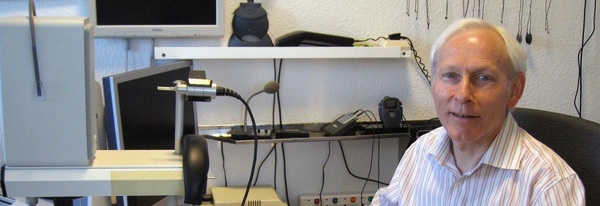 Älterer Mann sitzt an einem Schreibtisch mit Computer und Technik im Büro oder Labor.